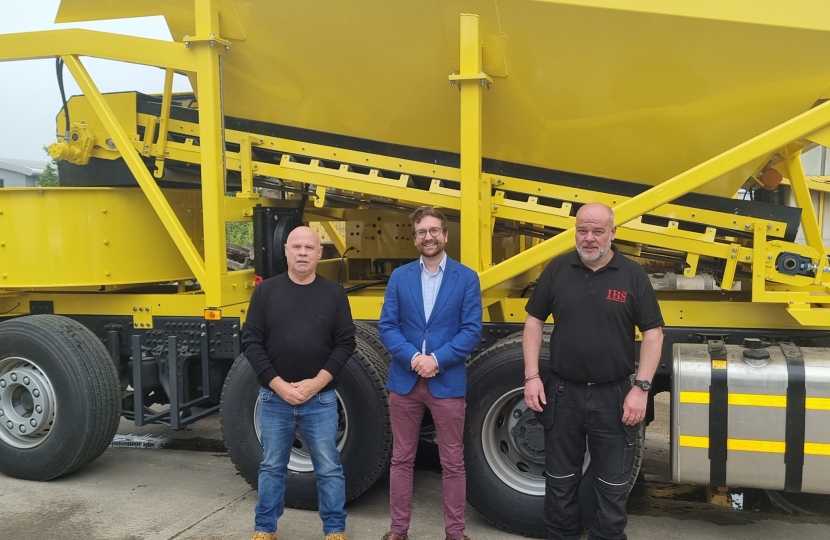 Alexander Stafford MP stands in front of a digger at Mixamate in Dinnington with two other people